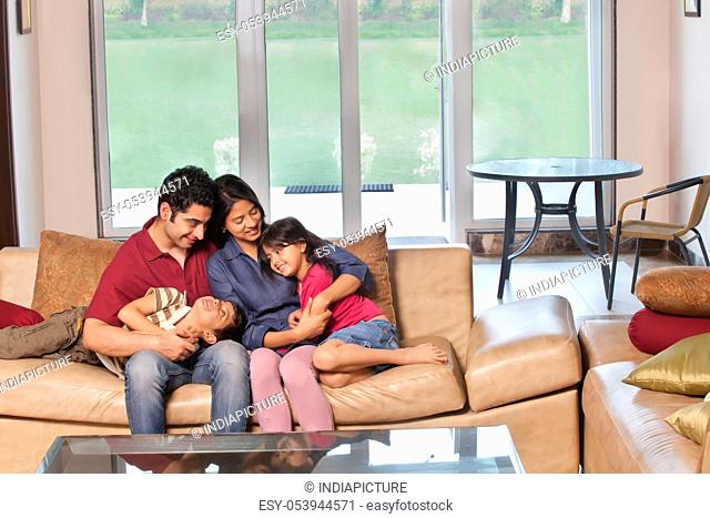 Parents sitting together with kids on sofa at home