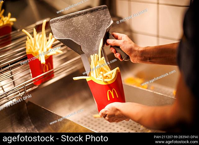 02 December 2021, Bavaria, Munich: An employee fills a bag with French fries at a branch of the McDonald's fast food chain on Martin-Luther-Strasse in Giesing