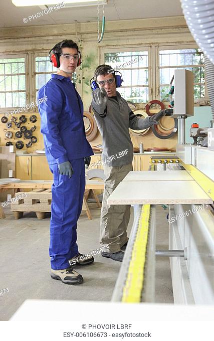 Carpenter and apprentice using industrial saw