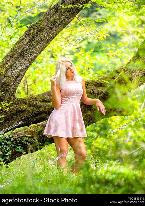 Attractive blonde woman daydreaming next to a big tree in forest