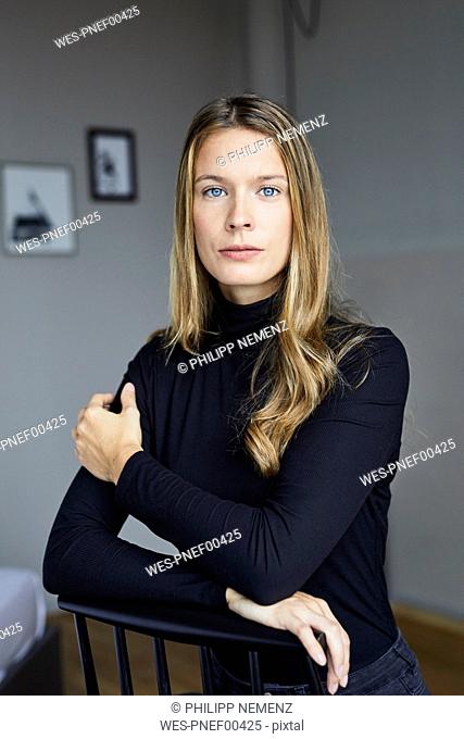 Portrait of young woman wearing black turtleneck sitting on chair