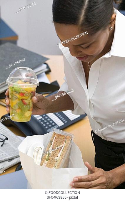 Woman with packed lunch sandwich, fruit salad in the office