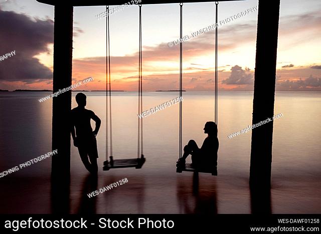 Couple on a swing at the sea at sunset, Maguhdhuvaa Island, Gaafu Dhaalu Atoll, Maldives