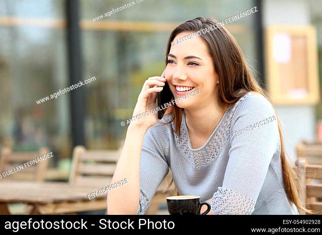 Happy young woman talking on the smart phone in a coffee shop terrace
