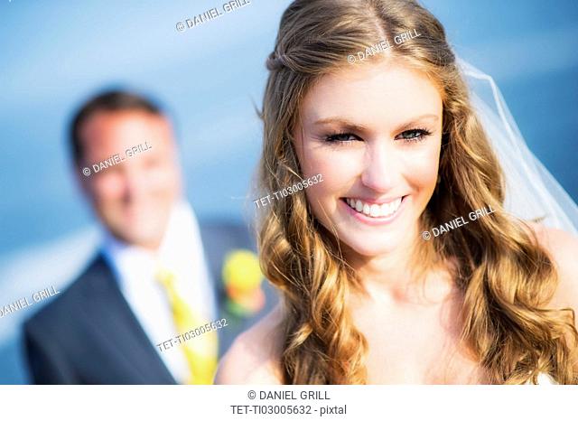 Portrait of smiling bride, groom in background