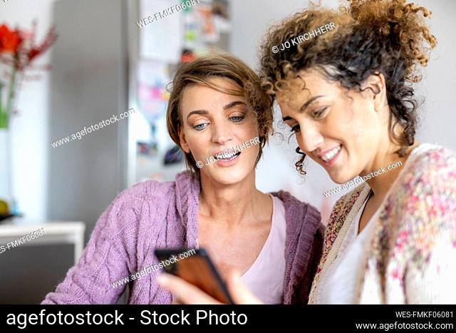 Two women looking at cell phone together at home