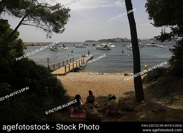22 July 2023, Spain, Calvia: People relax on the beach at Punta Negra in Mallorca, where several ships are anchored. According to a study