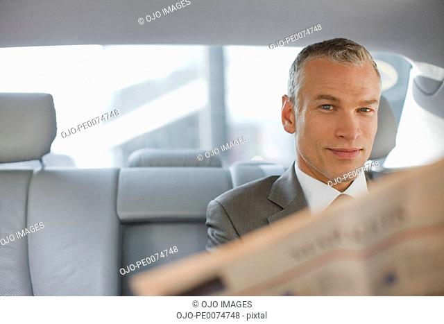 Businessman reading newspaper in back seat of car