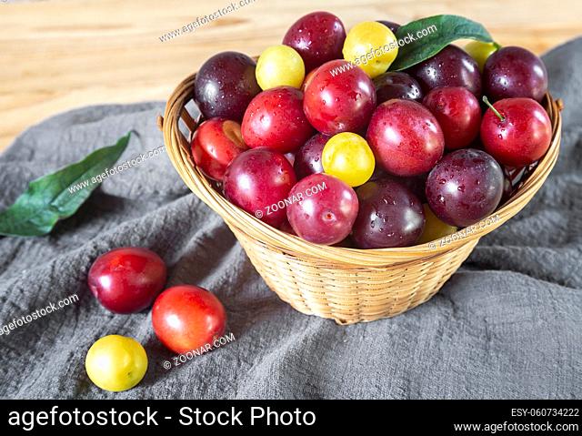 On the wooden table is a wicker basket filled with ripe large plums