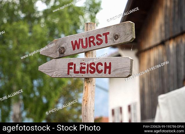 18 June 2023, Bavaria, Füssen: Two wooden signs pointing to a farm store selling sausage and meat stand near a farm near Füssen in the Allgäu region of Germany