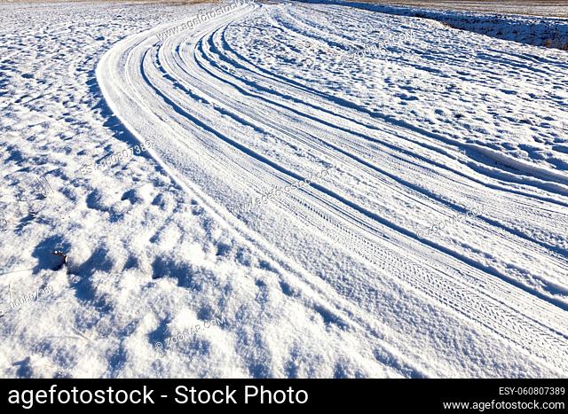 part of the snow-covered rural winding road in the field. There are traces of car tires. Close-up