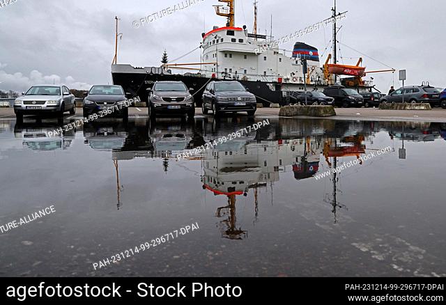 14 December 2023, Mecklenburg-Western Pomerania, Rostock: Cars and the icebreaker ""Stephan Jantzen"" are reflected in a large puddle in the city harbor