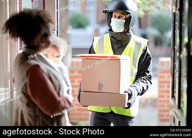 Woman receiving parcels from delivery man in face mask at front door