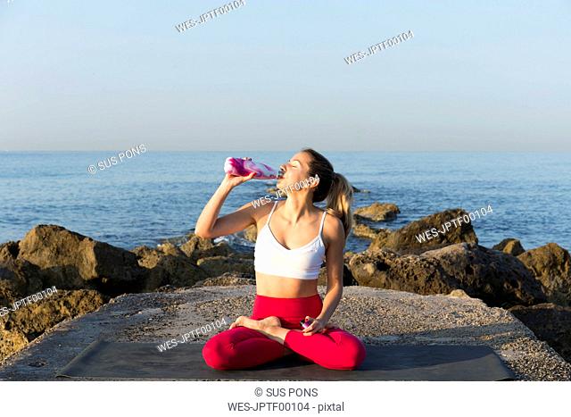 Young woman practicing yoga on the beach, drinking water