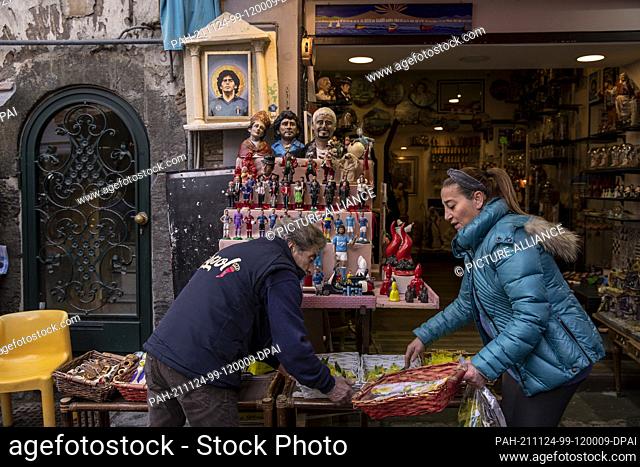 23 November 2021, Italy, Neapel: A man and a woman prepare a stand with sovereigns in the street San Gregorio Armeno, where also small and larger figures of the...