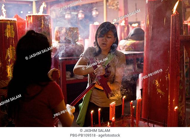 Woman lighting incense at traditional Chinese Buddhist temple Jakarta, Indonesia October 2010