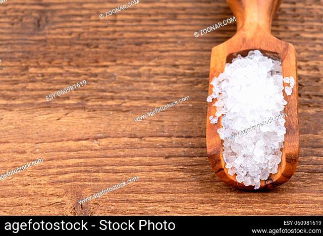 Rough crystal salt on a small spice shovel made of olive wood with copy space on a rustic wooden background