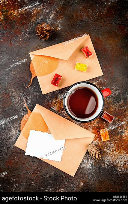 Enamel cups of tea, watercolors in cuvettes, two envelops, greetings card, autumn leaves and bumps on a rusty brown background