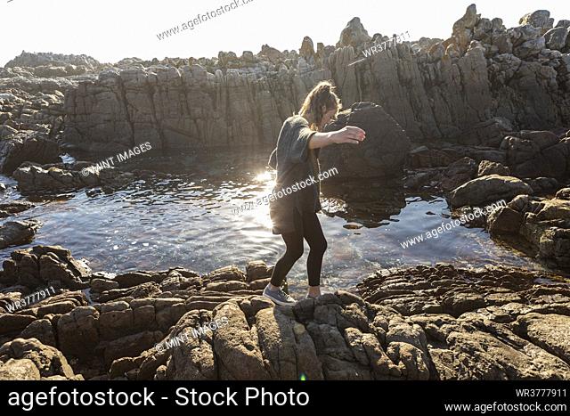 Teenage girl walking across jagged rocks, exploring rock pools by the ocean