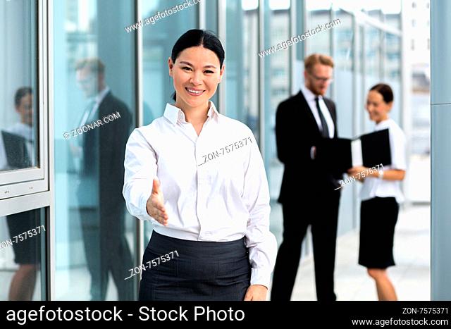Portrait of smiling businesswoman. Businesswoman giving a handshake, her collegues speaking about problems on the background
