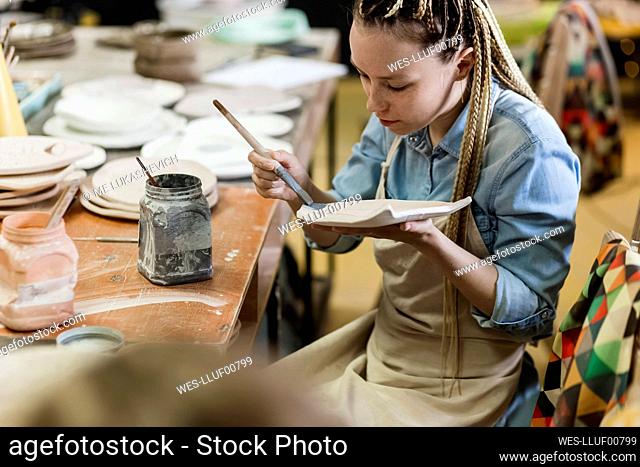 Craftsperson painting earthen plate at workshop