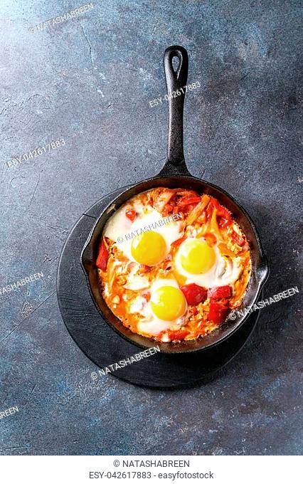 Traditional Israeli Cuisine dishes Shakshuka. Fried egg with vegetables tomatoes and paprika in cast-iron pan on wooden board over blue texture background