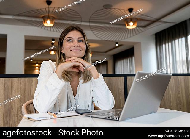 Smiling businesswoman sitting with hand on chin at restaurant