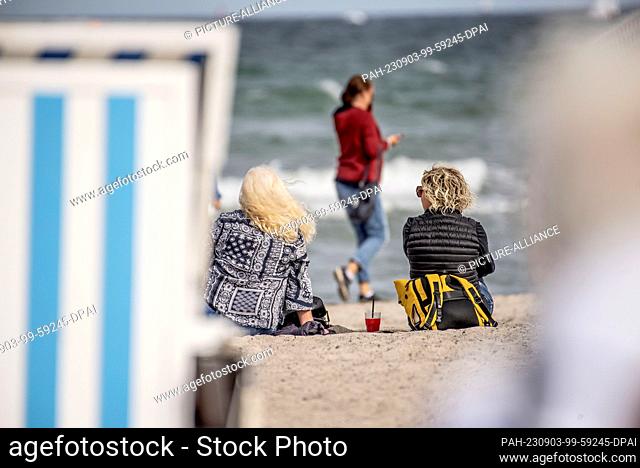 03 September 2023, Mecklenburg-Western Pomerania, Rostock Warnemünde: Two women sit between the beach chairs on the Baltic Sea beach of Warnemünde