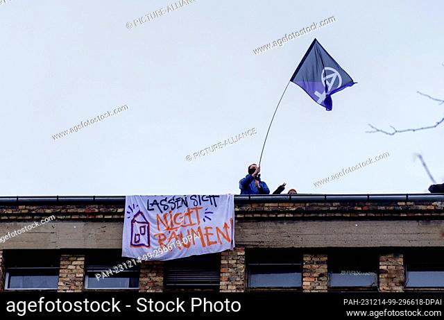 14 December 2023, Hesse, Frankfurt/Main: An activist stands with a flag on the roof of the Dondorf printing works with a banner reading ""Do not allow yourself...