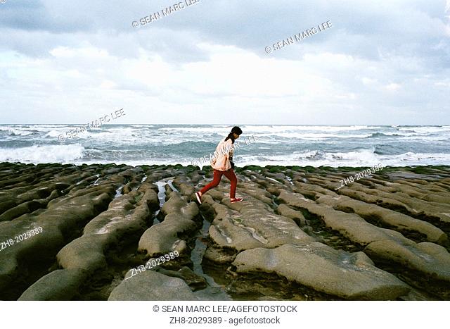 A girl hops across rock formations on the coast of Lao Mei Beach in Taiwan