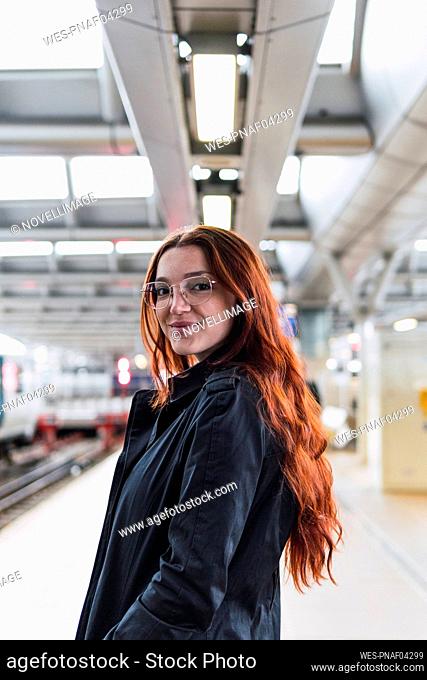 Happy redhead woman standing at railroad station platform
