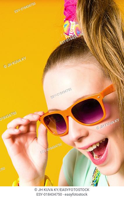 Beautiful girl wearing sunglasses, expressing faces, yellow background
