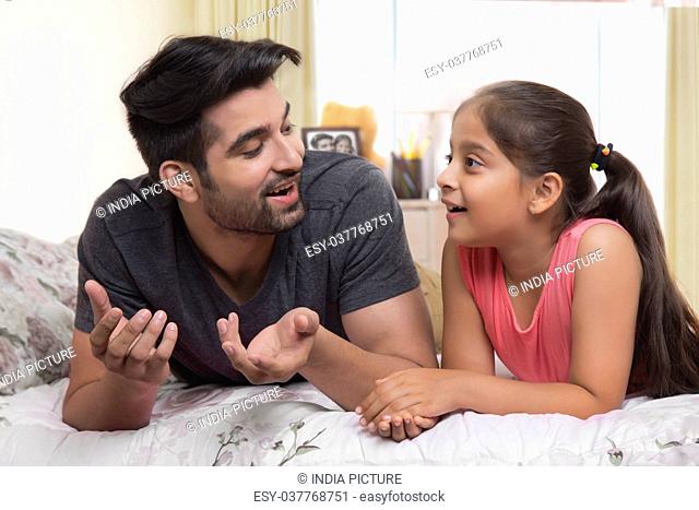 Father and daughter lying on bed and talking