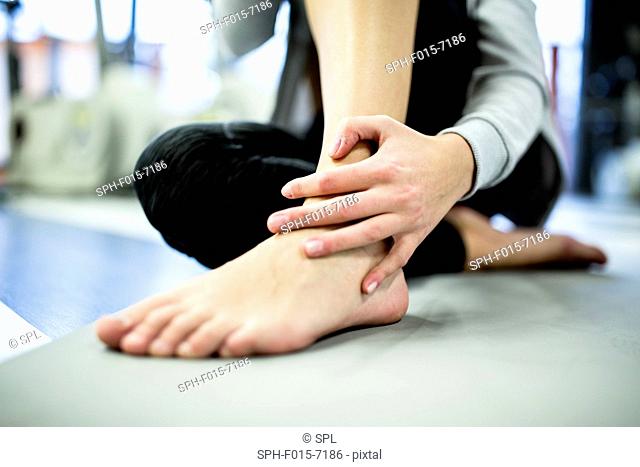 MODEL RELEASED. Young woman massaging ankle in gym