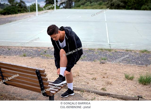 Male teenage basketball player fastening trainers by basketball court