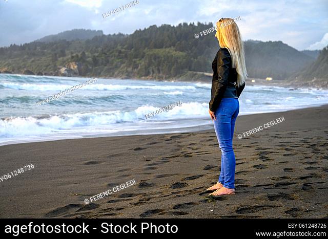 Bright portrait of an attractive blonde woman standing by the ocean somewhere at the shores of Northern California, United States of America