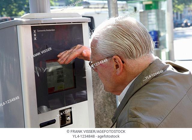 Elderly man tries to read the information on the display of a parking meter, Amsterdam, Netherlands
