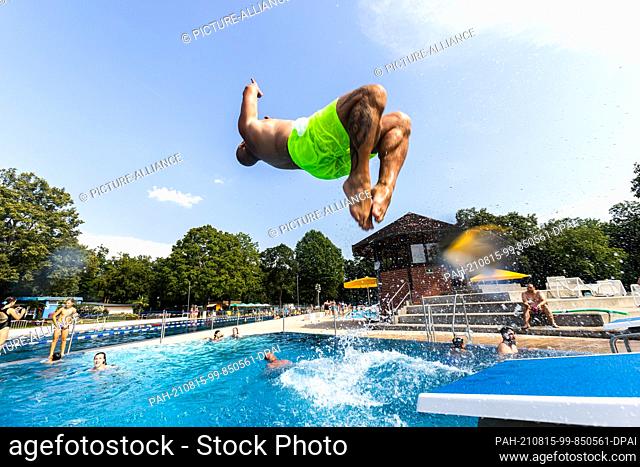 15 August 2021, Baden-Wuerttemberg, Breisach am Rhein: A man does a backflip into a pool at Breisach's Waldschwimmbad. Temperatures around 30 degrees attract...