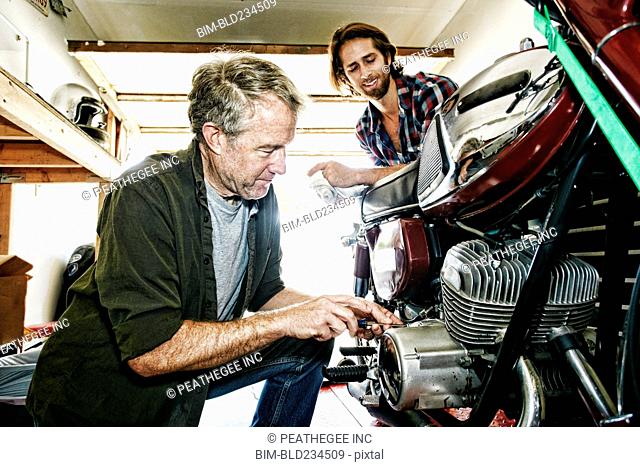 Caucasian son watching father repairing motorcycle in garage