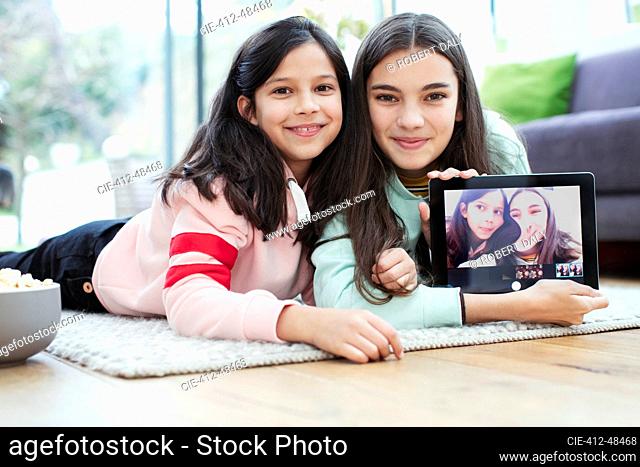 Portrait smiling sisters using digital tablet camera on living room floor