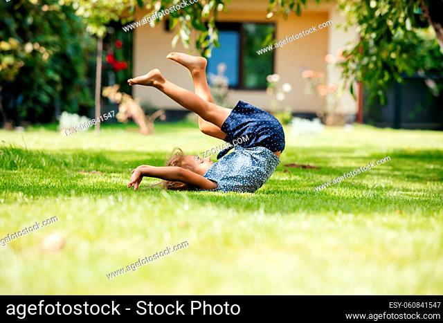 Active little girl makes a somersault on a green lawn