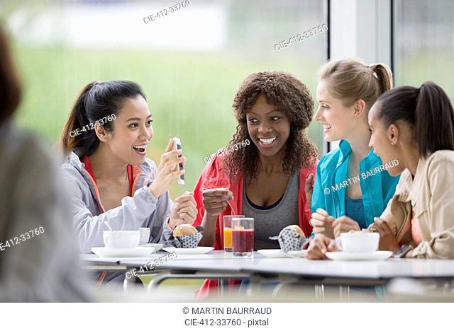 Smiling women drinking coffee and juice using cell phone in cafe post workout