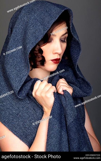 Beauty portrait of brunette woman dressed in dark blue scarf. Female portrait from a three-quarter angle on black background. Hand wraps the scarf
