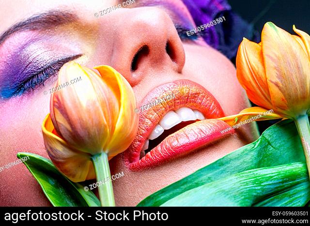 closeup of beautiful young woman with orange lips and yellow tulip flowers touching them. purple eye shadows