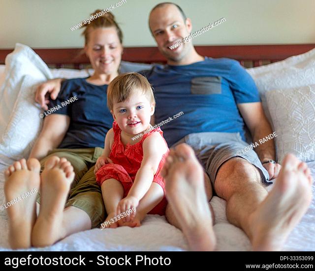 A young family spends time together relaxing on a bed and looking into the camera with the focus on the young girl, Pineacre on the Lake Bed and Breakfast;...
