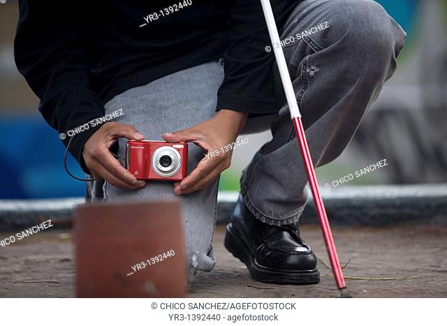 A blind photographer takes pictures as he kneels
