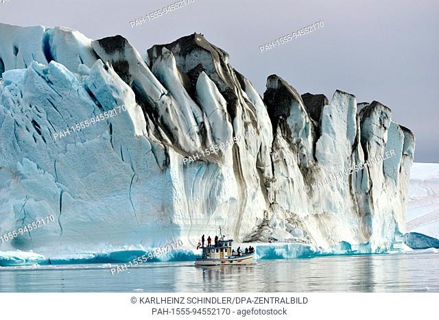 A fishing boat with tourists on board makes its way between icebergs floating in the fjord near Ilulissat on the west coast of Greenland