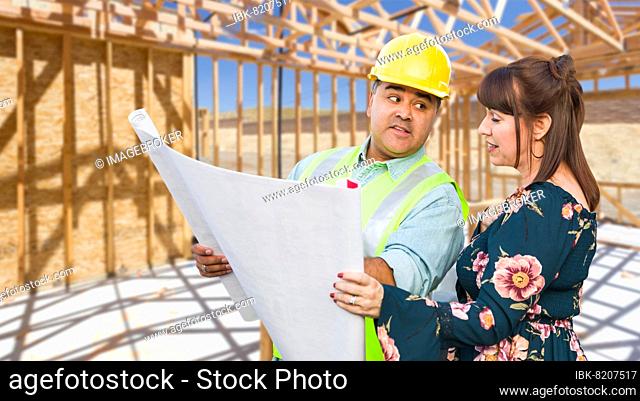 Hispanic male contractor talking with female client over blueprint plans at construction site