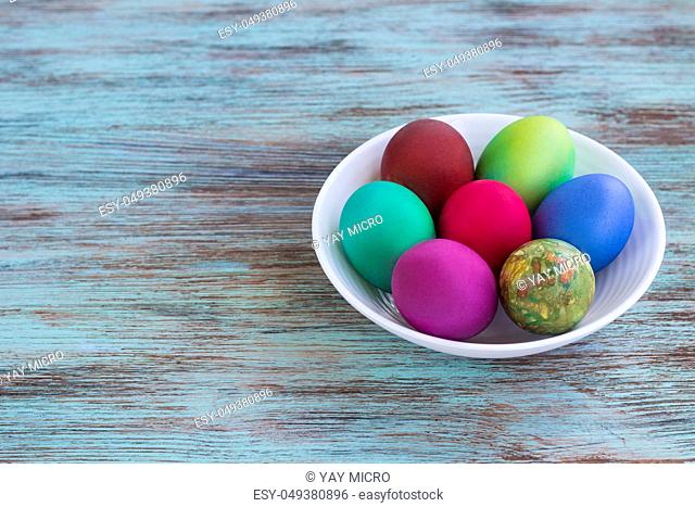 White plate of Easter multicolored boiled eggs decoration on wooden background
