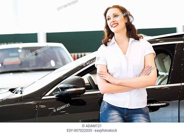 portrait of a young woman stands with his arms crossed over his chest in the cars showroom